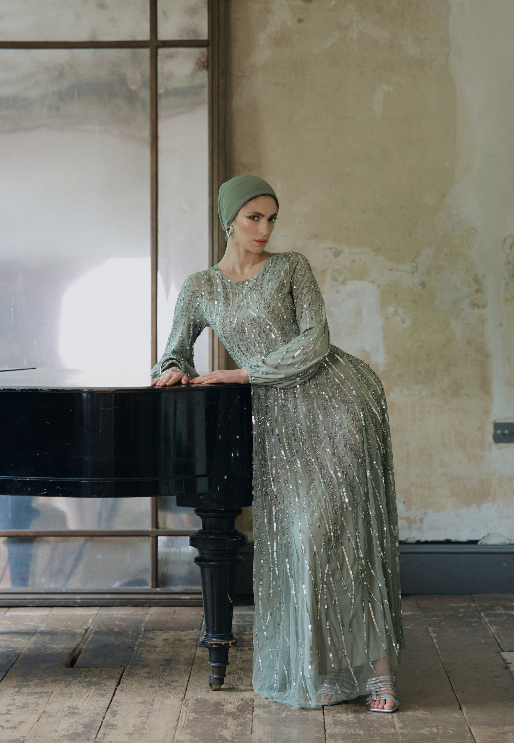 Woman in a sparkling green dress standing next to a grand piano in an indoor setting.