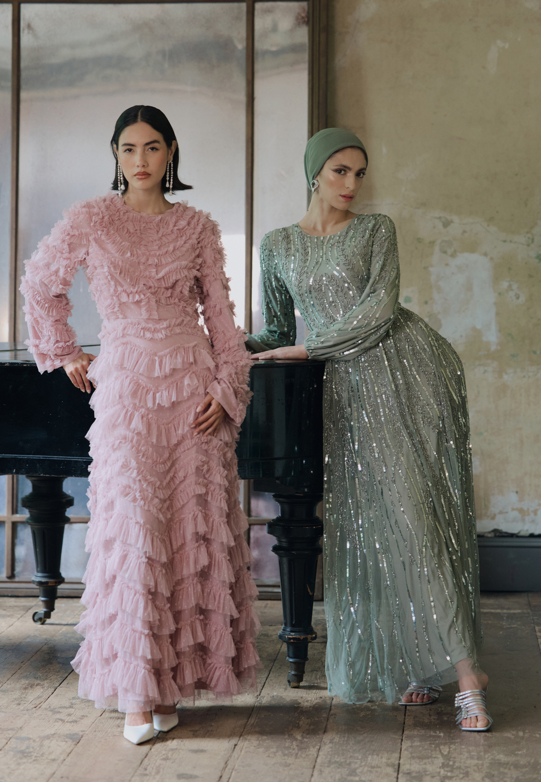 Two women in elegant dresses standing indoors with a piano in the background.