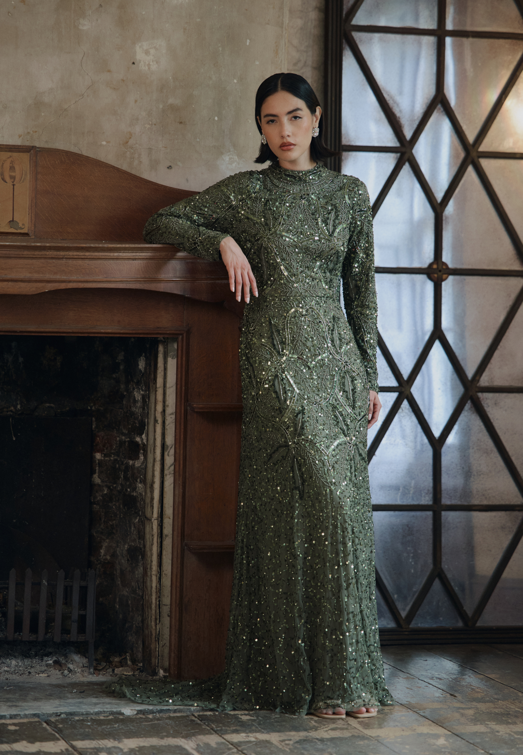 Woman in a green dress standing in a room with a fireplace and geometric window.