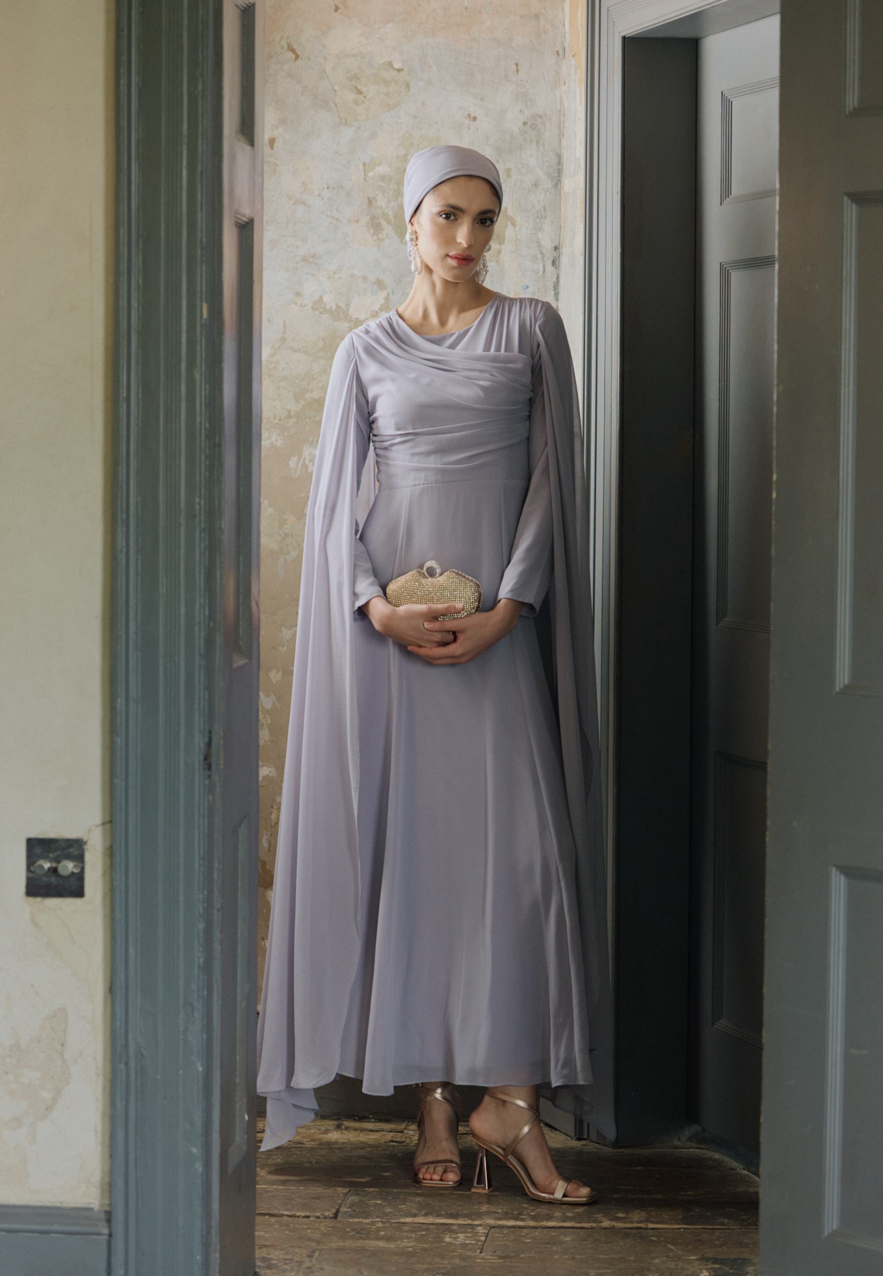 Woman in a long, light gray dress standing in a doorway.