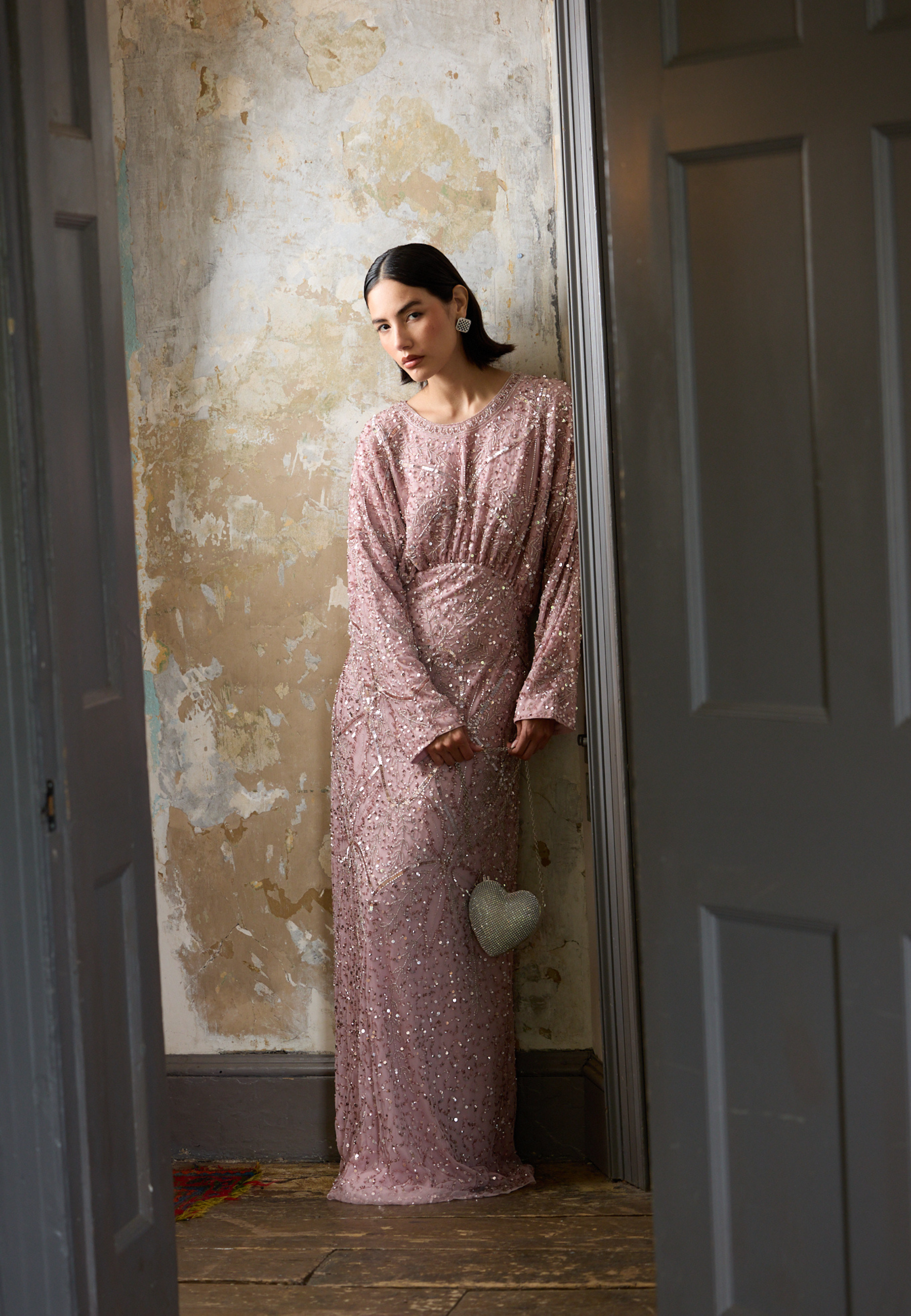 Woman in a pink dress standing in a doorway with peeling paint on the wall.