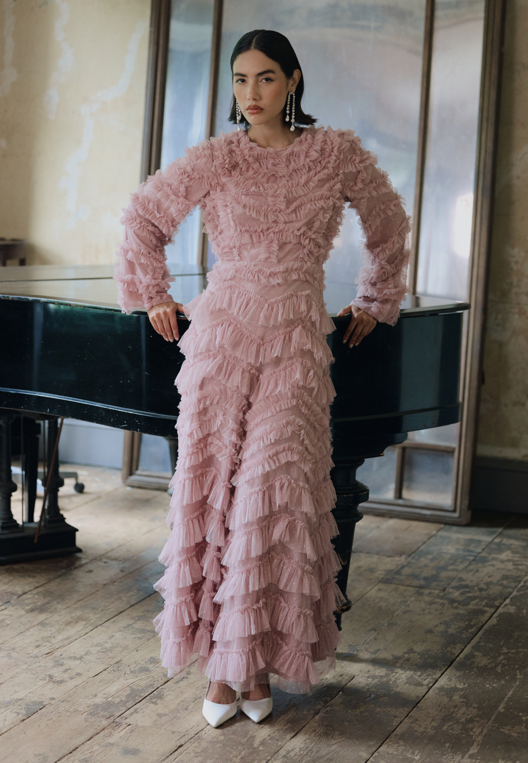 Woman in a pink ruffled dress standing in a room with a piano.