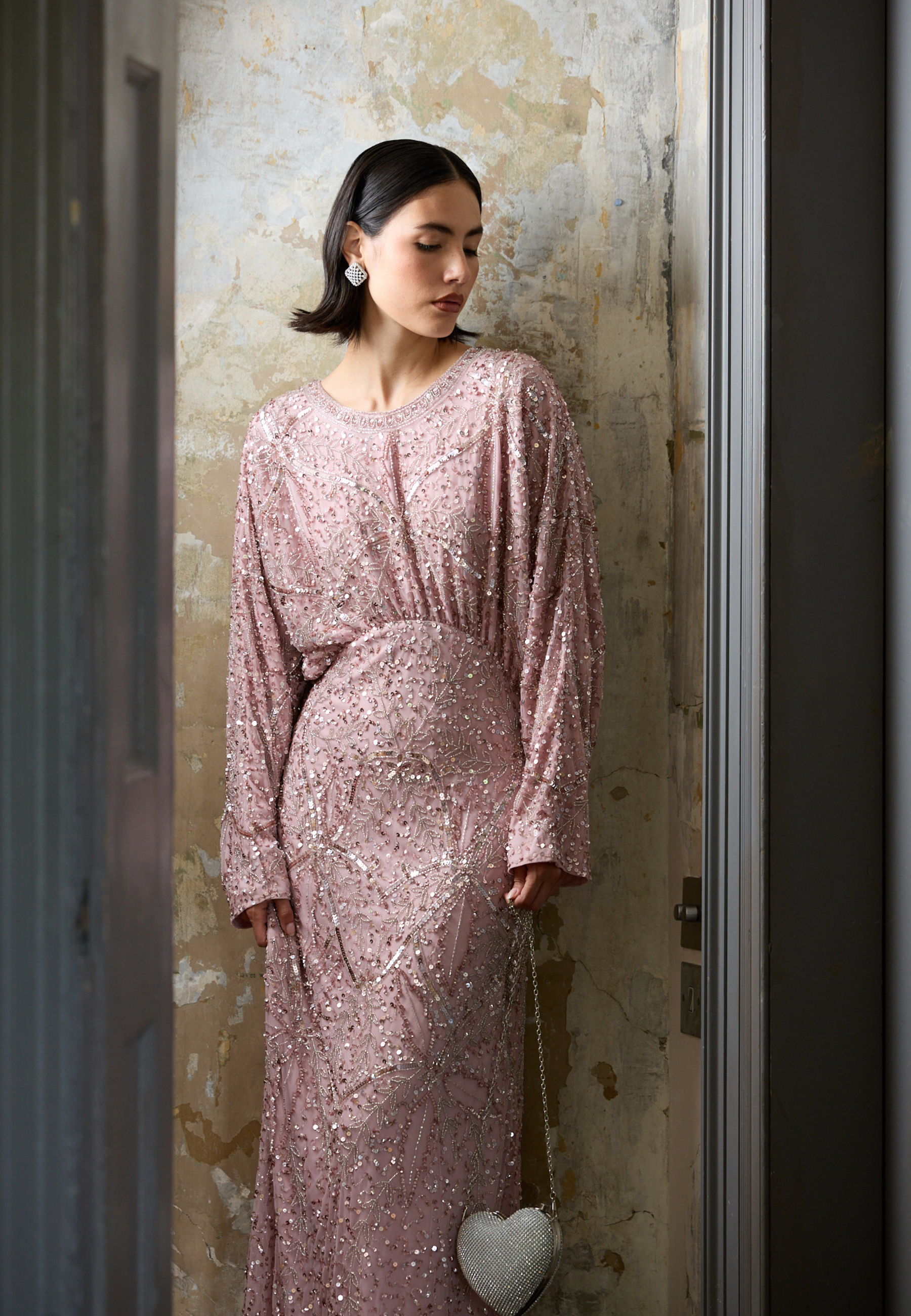 Woman wearing a pink sequin dress standing against a textured wall.