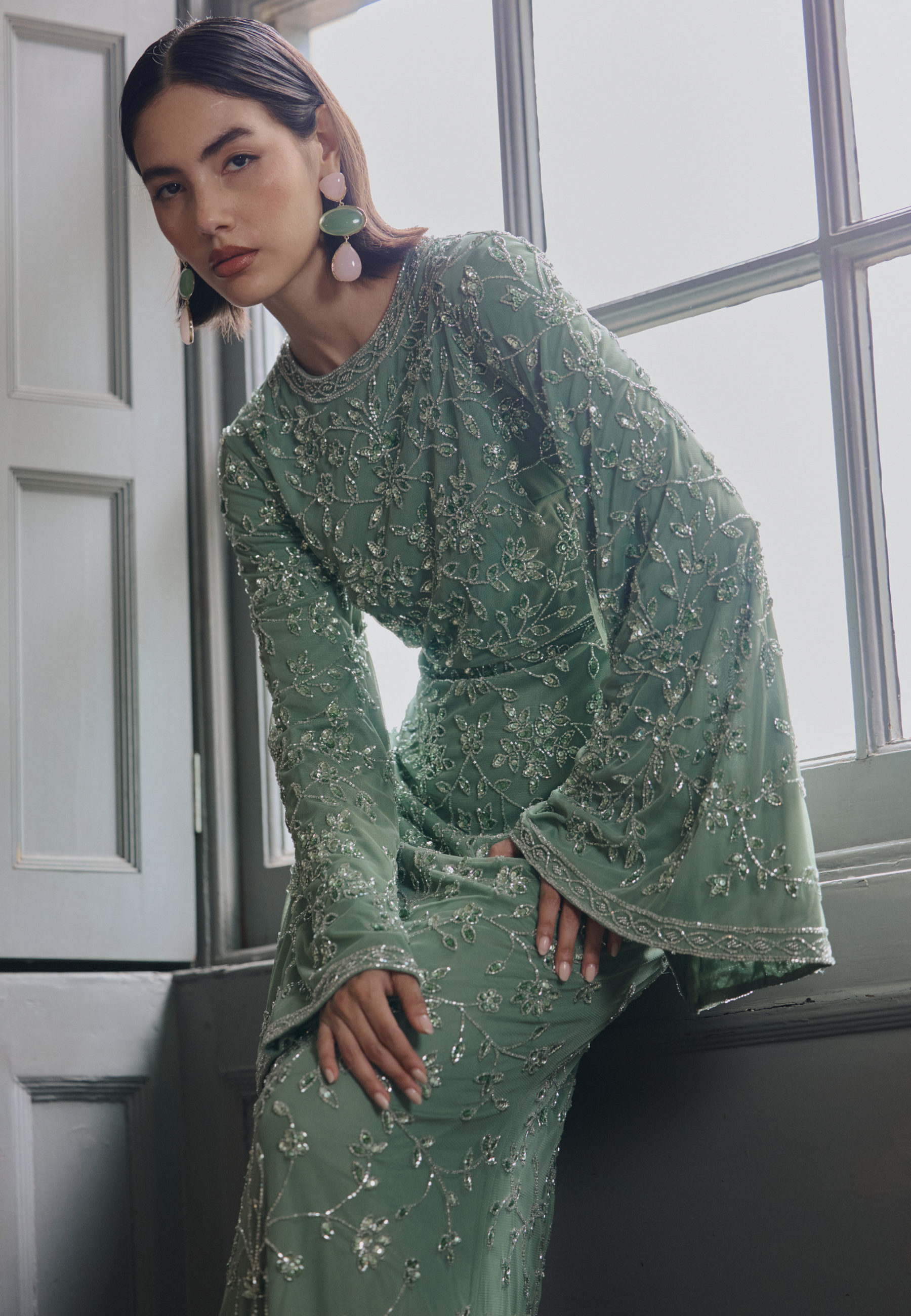 Woman in a green dress with floral patterns sitting indoors.