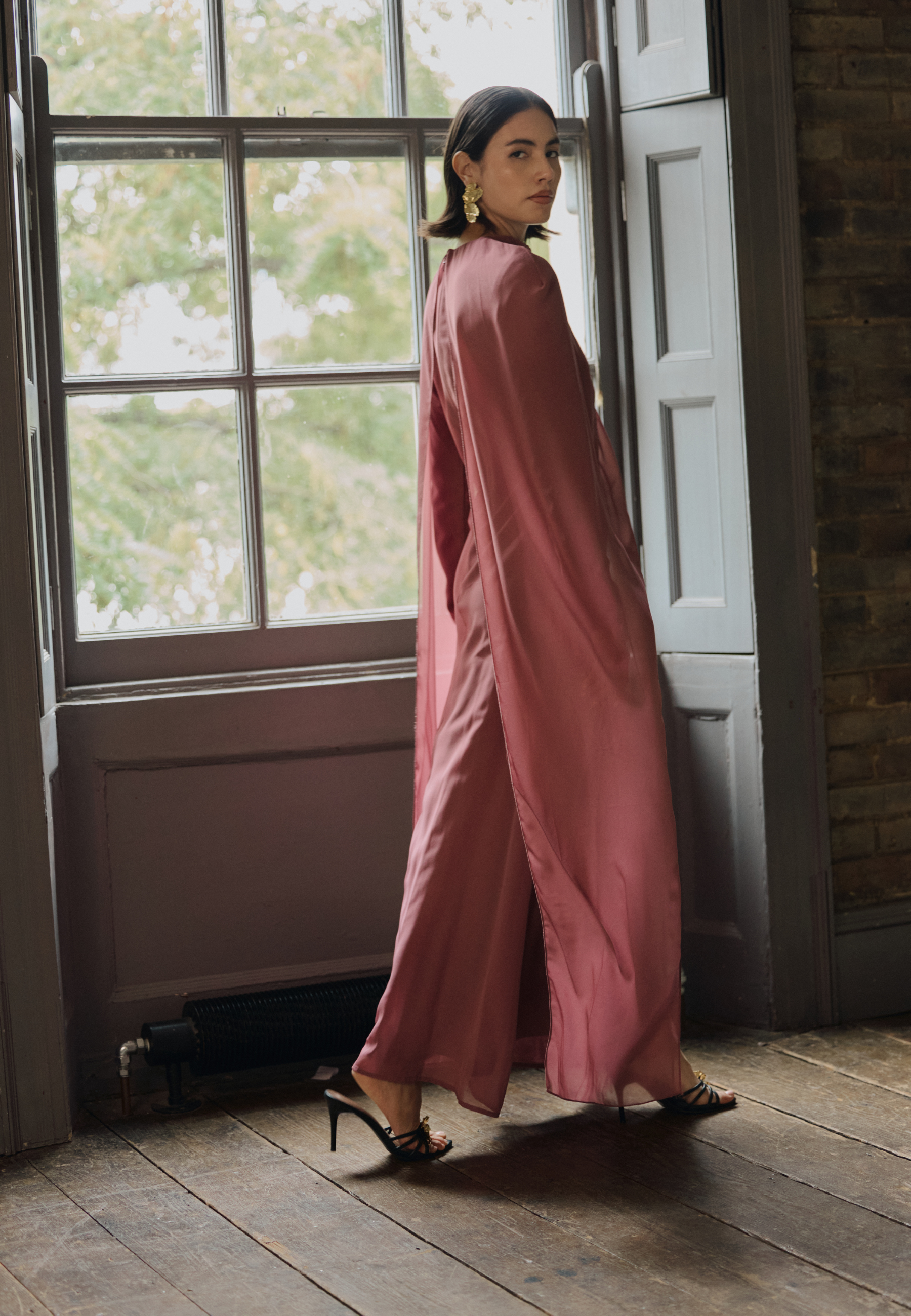 Woman in a pink outfit standing in a room with large windows.