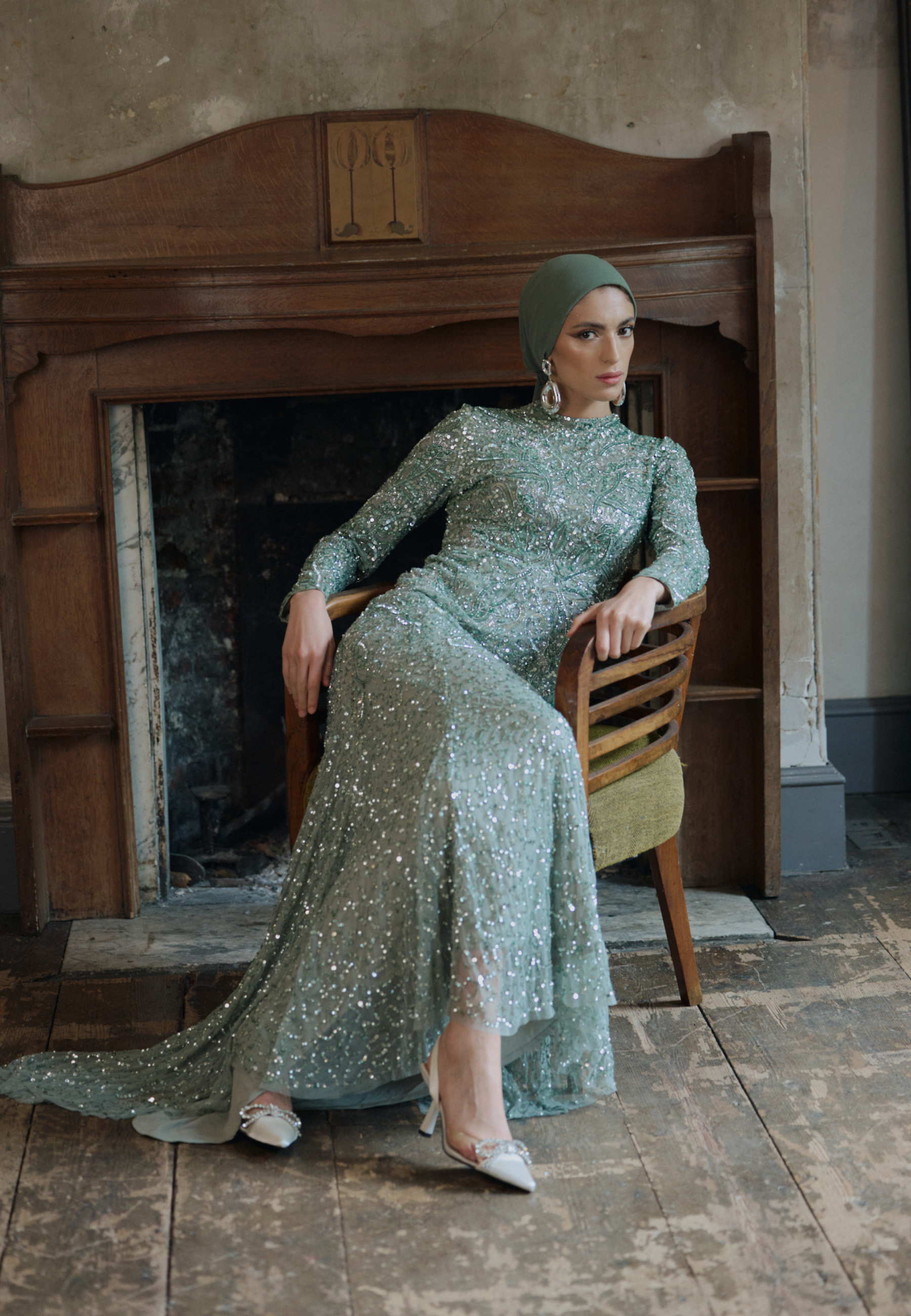 Woman in a sparkly green dress sitting in front of a fireplace.
