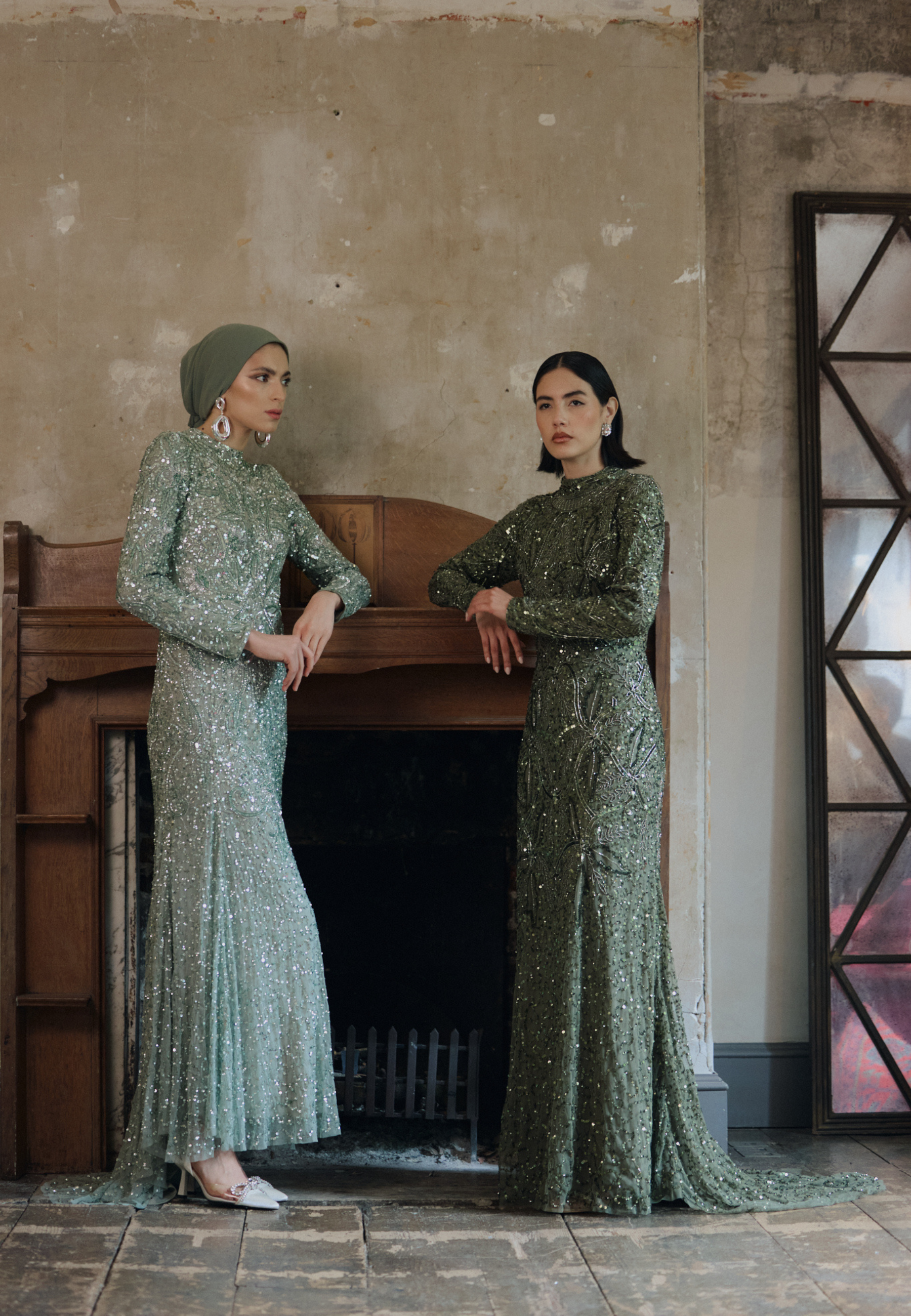 Two women in green dresses standing in a room with a fireplace.