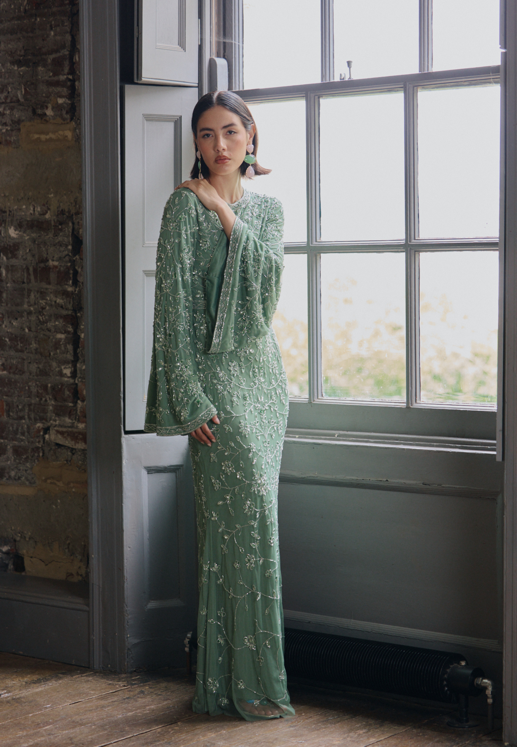 Woman in a green dress standing by a window with a brick wall background