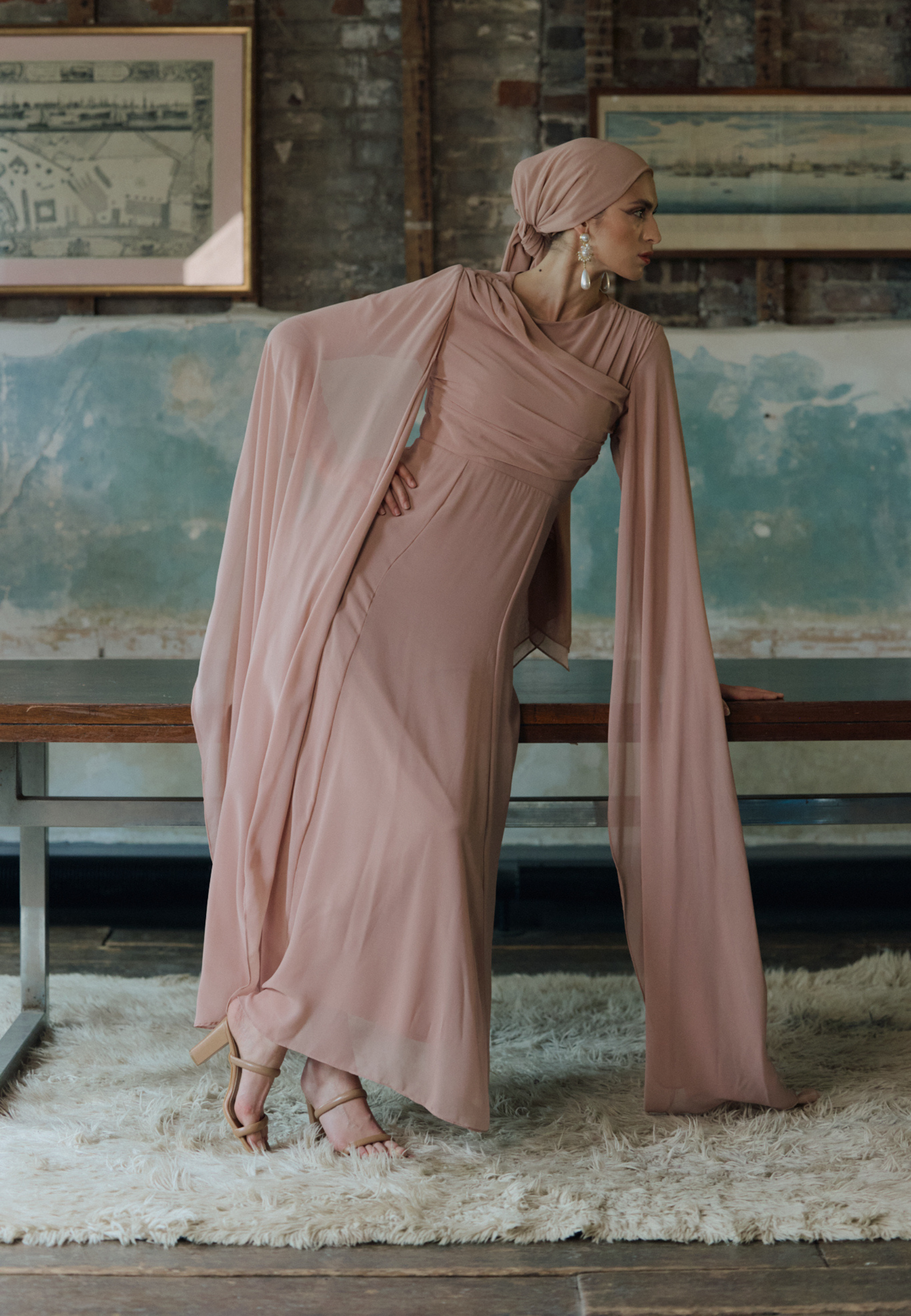 Woman in a long, light brown dress standing in a room with rustic decor.