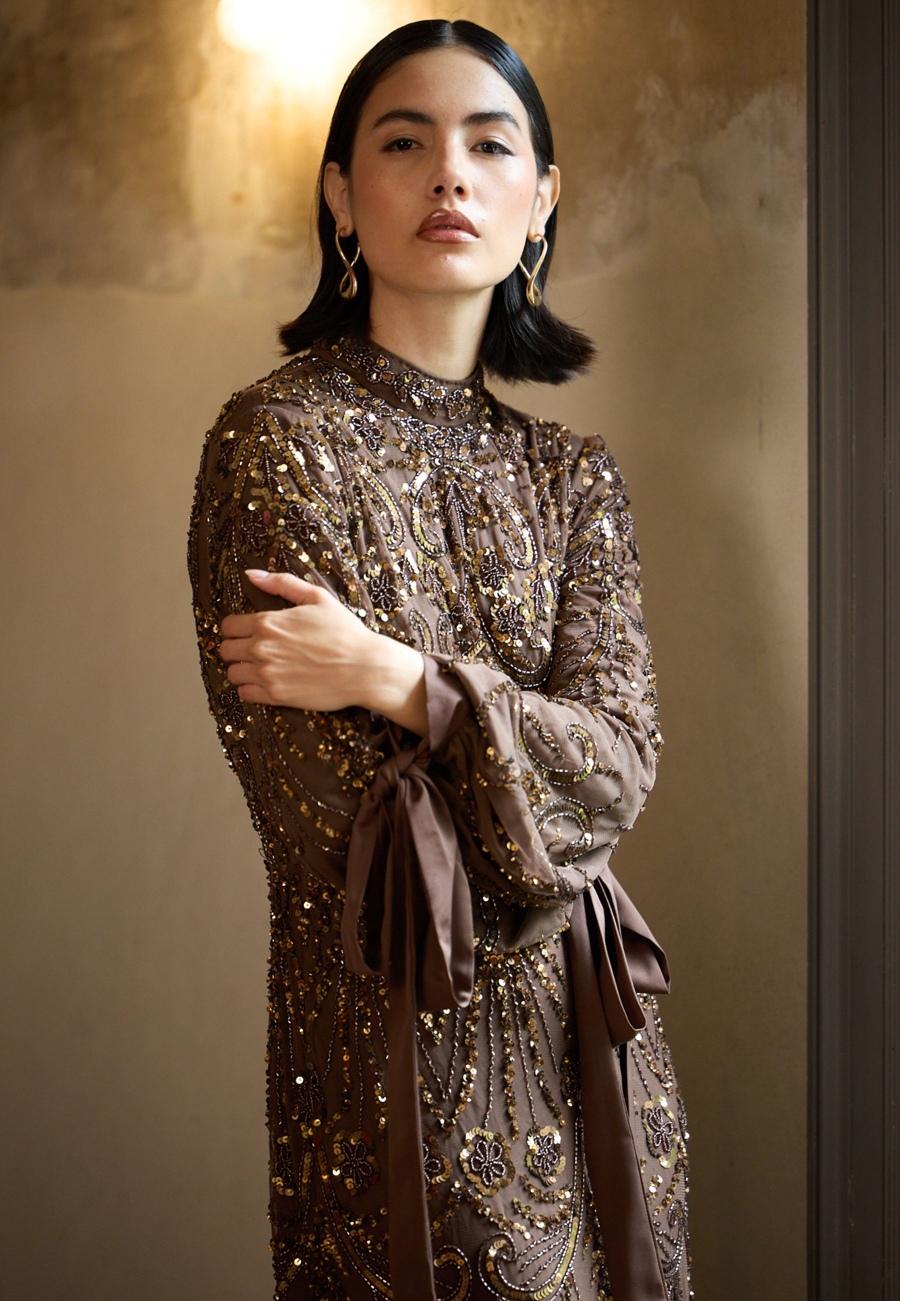Woman wearing a brown sequined dress against a beige wall.