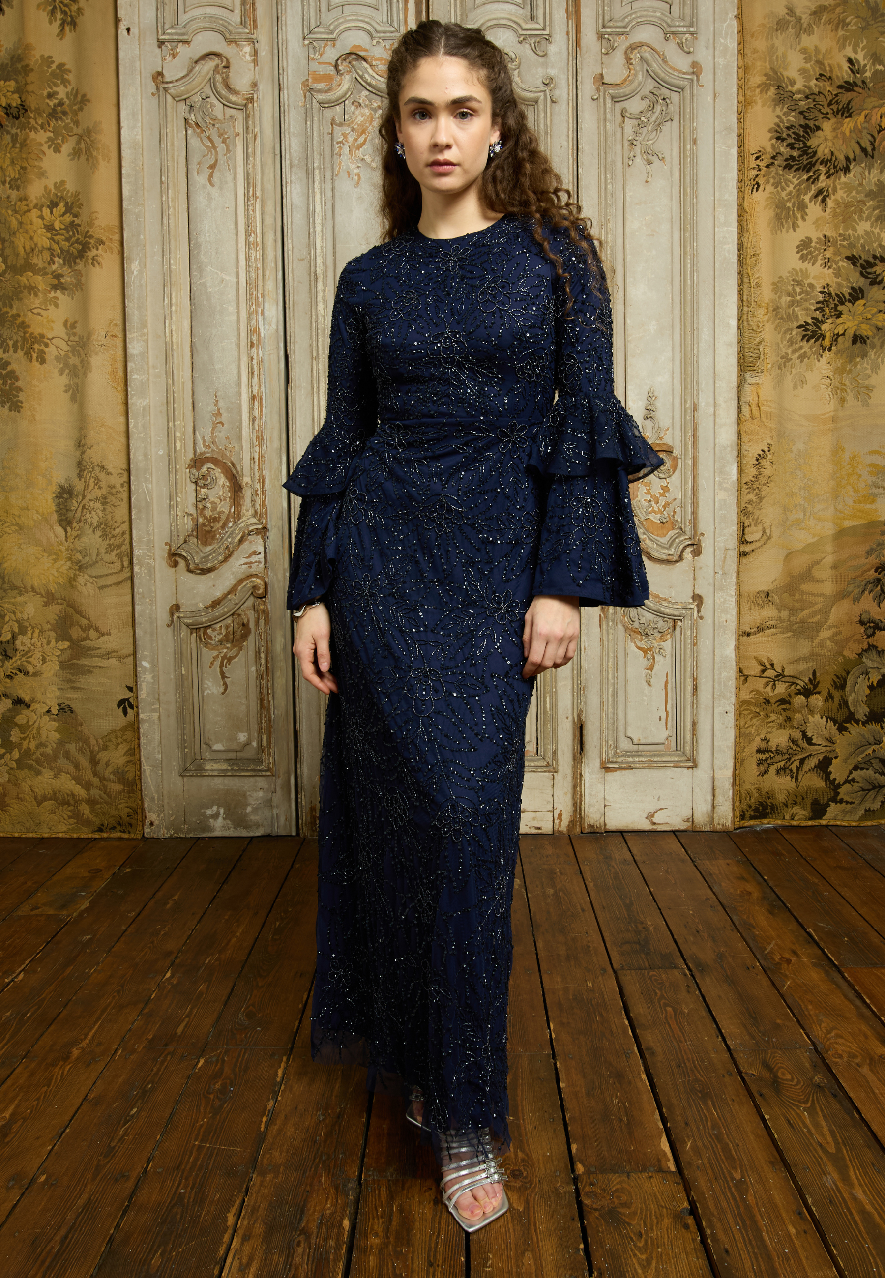 A woman modeling a midnight blue embellished sequin maxi dress with long sleeves and a round neckline.