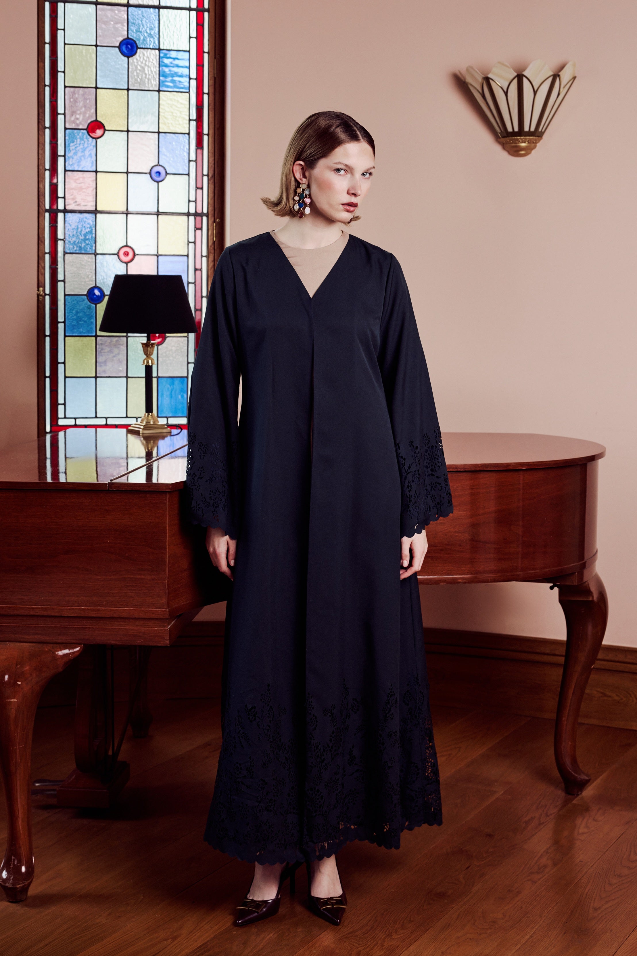 Woman in a dark blue dress standing in a room with a stained glass window and wooden furniture.
