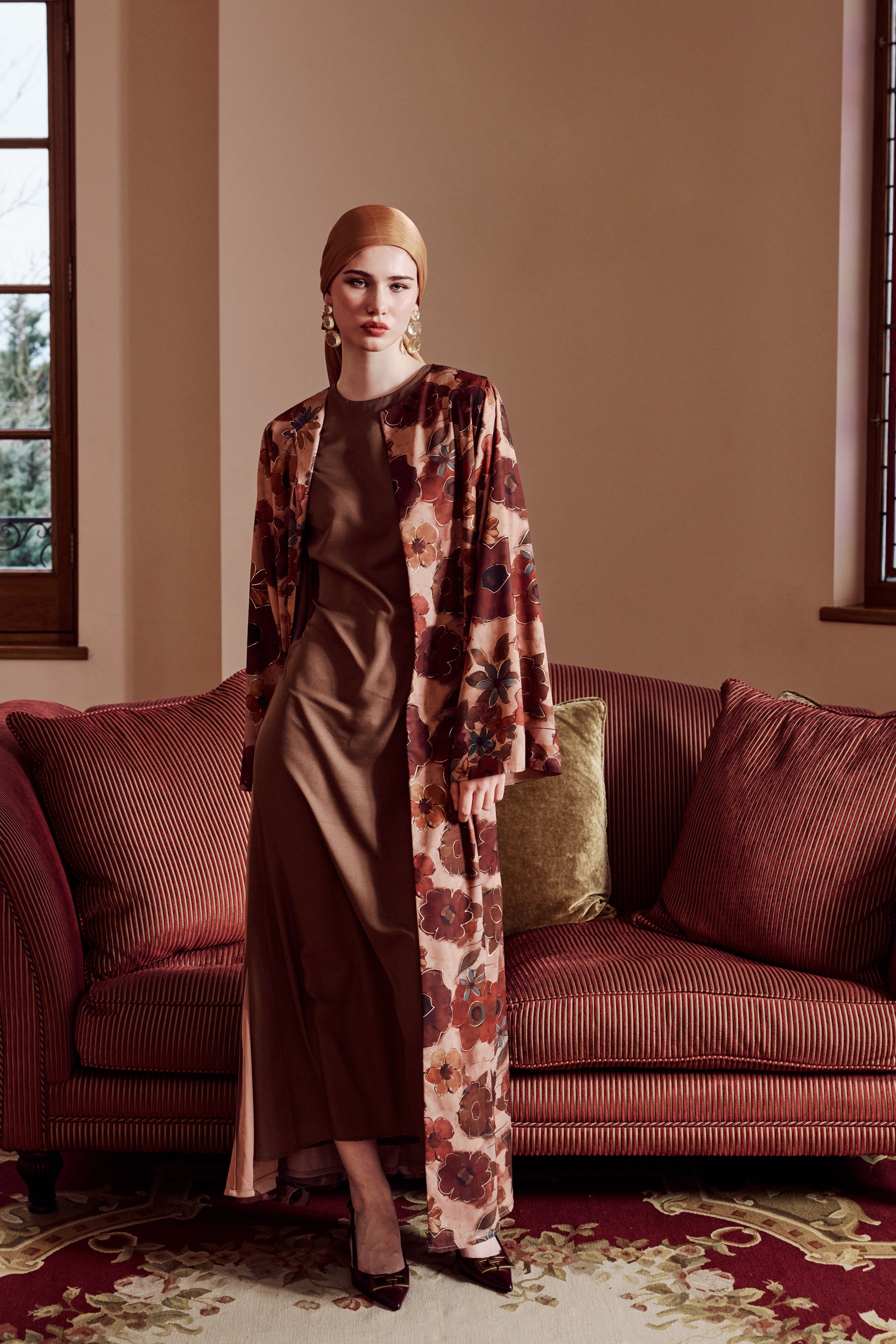 Woman in a patterned outfit standing in a room with a couch and windows.