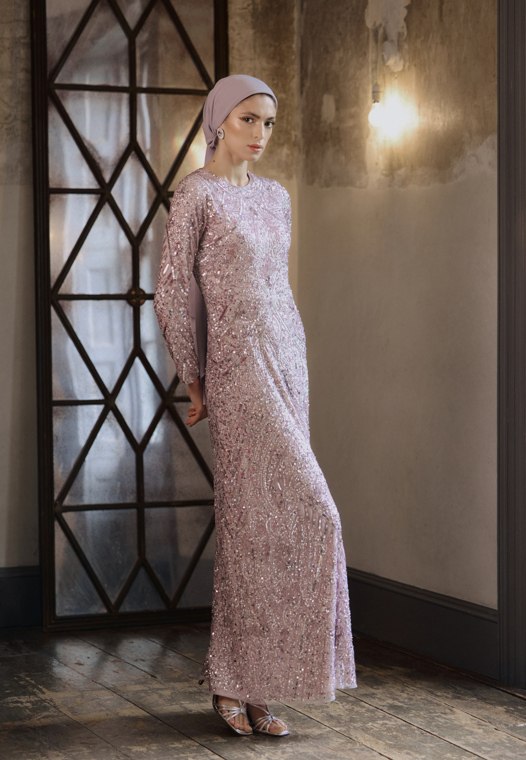 Woman in a long, floral-patterned dress standing in a room with geometric window design.
