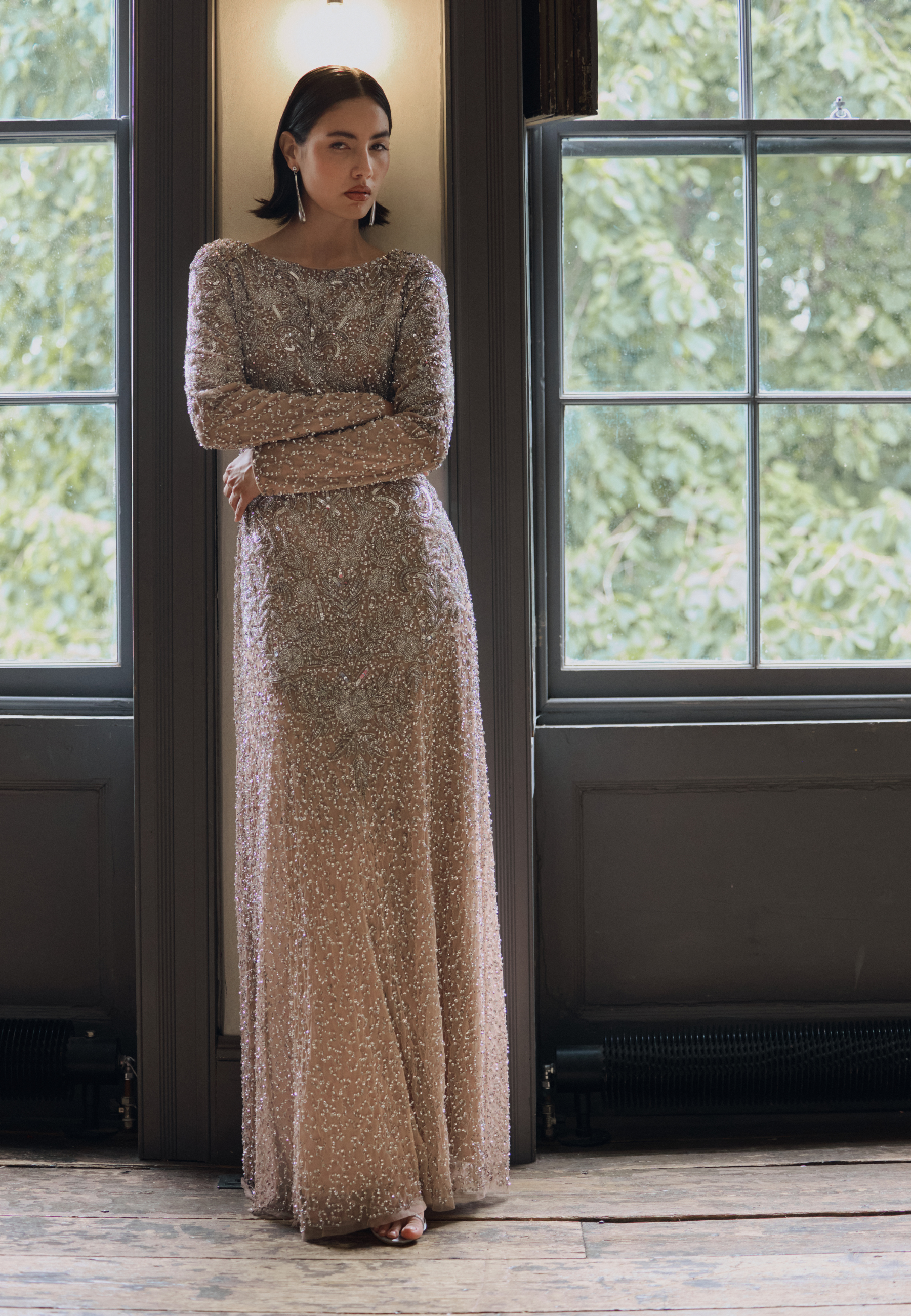 Woman in a long, sparkly dress standing in a room with large windows.